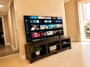 A flat-screen TV mounted on a dark wooden stand with a 'Welcome' sign, displaying a streaming service interface with various content options.