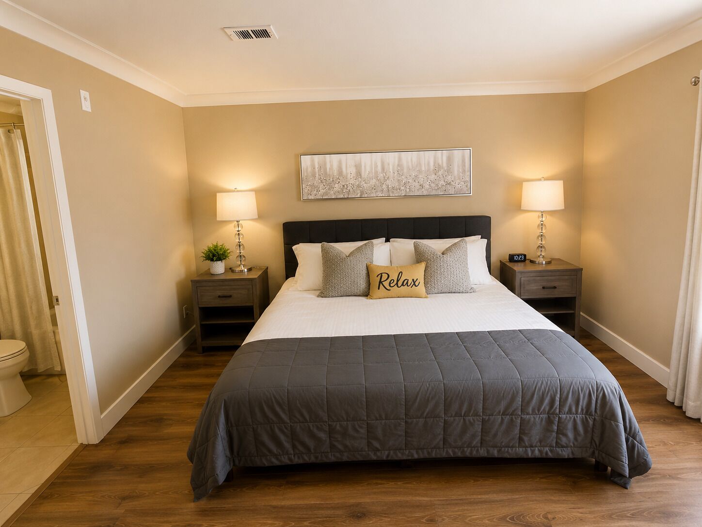 A bedroom with a large bed, two bedside tables with lamps, a wall clock, and a framed artwork above the bed.