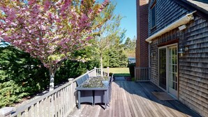 Une terrasse en bois avec une table et des chaises, un bâtiment en briques doté de grandes fenêtres et un arbre aux fleurs roses.