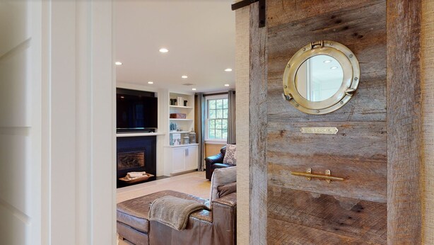 Un salon chaleureux avec une cheminée, un canapé en cuir et une porte en bois ornée d’un miroir rond.