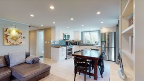 Une cuisine moderne avec des meubles blancs, des appareils en acier inoxydable et un coin repas comprenant une table et des chaises en bois.