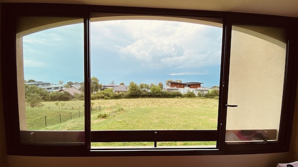 A window with a view of a grassy field, a few houses, and a clear sky.