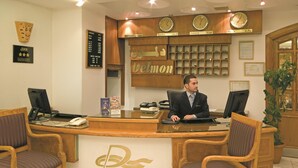 En receptionsdisk med en man sittande bakom den, omgiven av trästolar och en klocka på väggen ovanför.