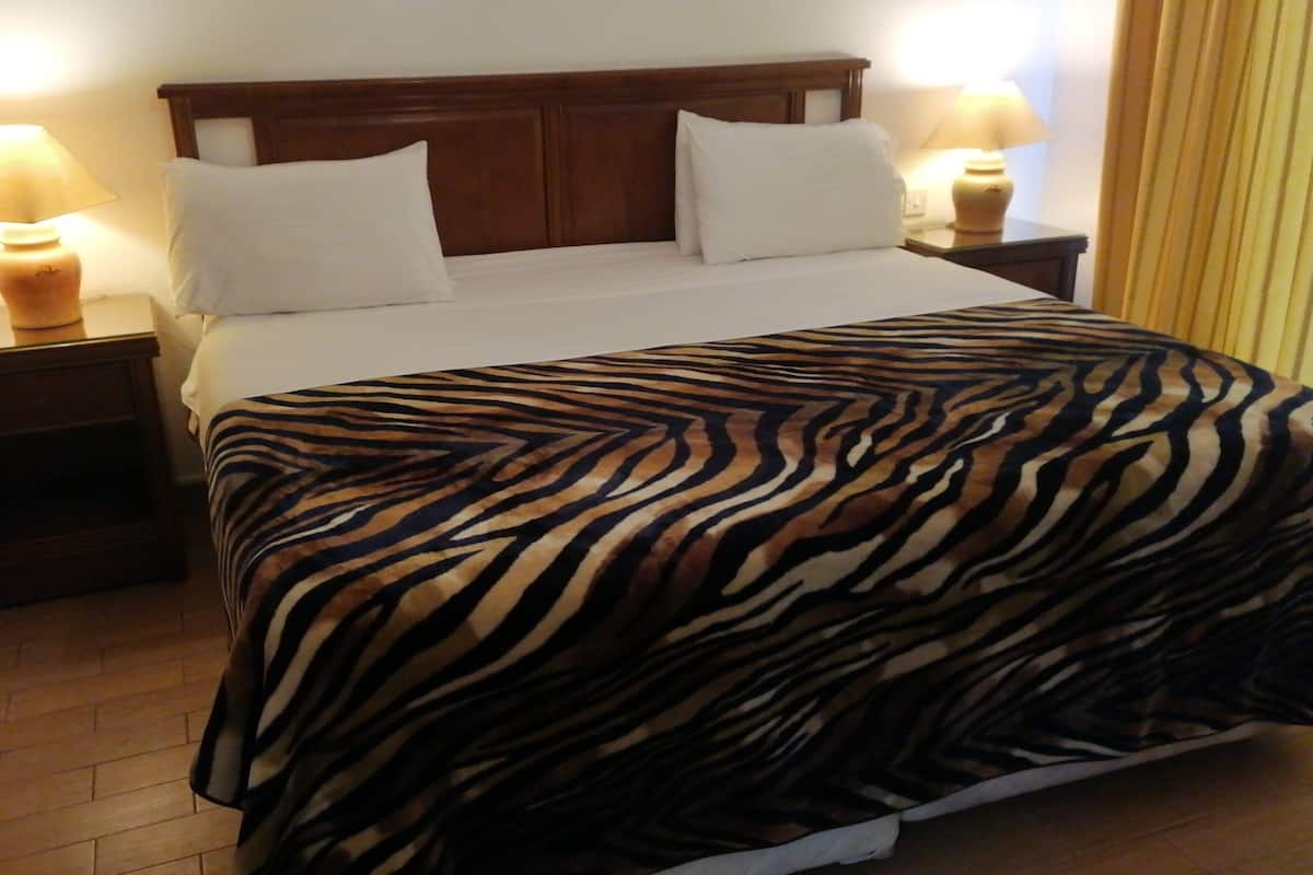 A hotel room with a wooden headboard, white bedding, and a zebra-patterned bedspread. There are two bedside lamps and a nightstand with a lamp.