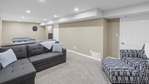 A modern living room with a grey sectional sofa, a patterned ottoman, and a dartboard on the wall. - Knock's Hot Tub Haven in Loveland (Loveland)