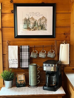 Cozy cabin retreat with a framed quote by John Muir, a coffee station, and a potted plant.