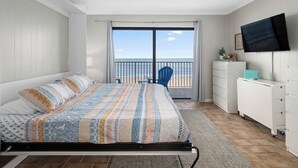 A bedroom with a bed, a TV, a desk, and a balcony with a view. - Oceanfront Studio, King bed, Sleeps 4, Pool, Wi-Fi (Ocean City)