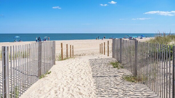 A sandy beach path leading to the sea, with a wooden fence on one side and beach umbrellas on the other. - Oceanfront Studio, King bed, Sleeps 4, Pool, Wi-Fi (Ocean City)