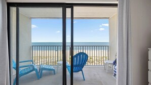 A balcony with a view of the beach, featuring blue chairs and a small table. - Oceanfront Studio, King bed, Sleeps 4, Pool, Wi-Fi (Ocean City)