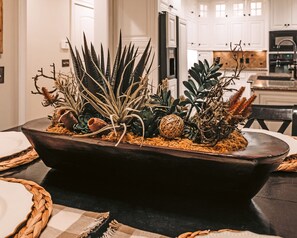 Una jardinera de madera oscura con diversos suculentos y elementos decorativos sobre una mesa de comedor.