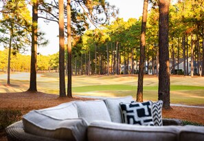 A view of a golf course with tall pine trees and a house in the background.