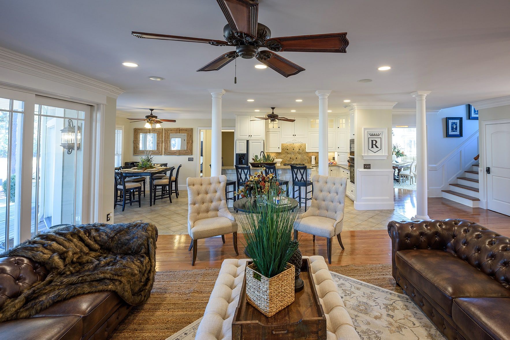 A spacious living room with a high ceiling fan, leather sofas, and a central coffee table.