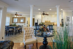 A spacious living room with a dining area, a kitchen, and a large window with blinds.