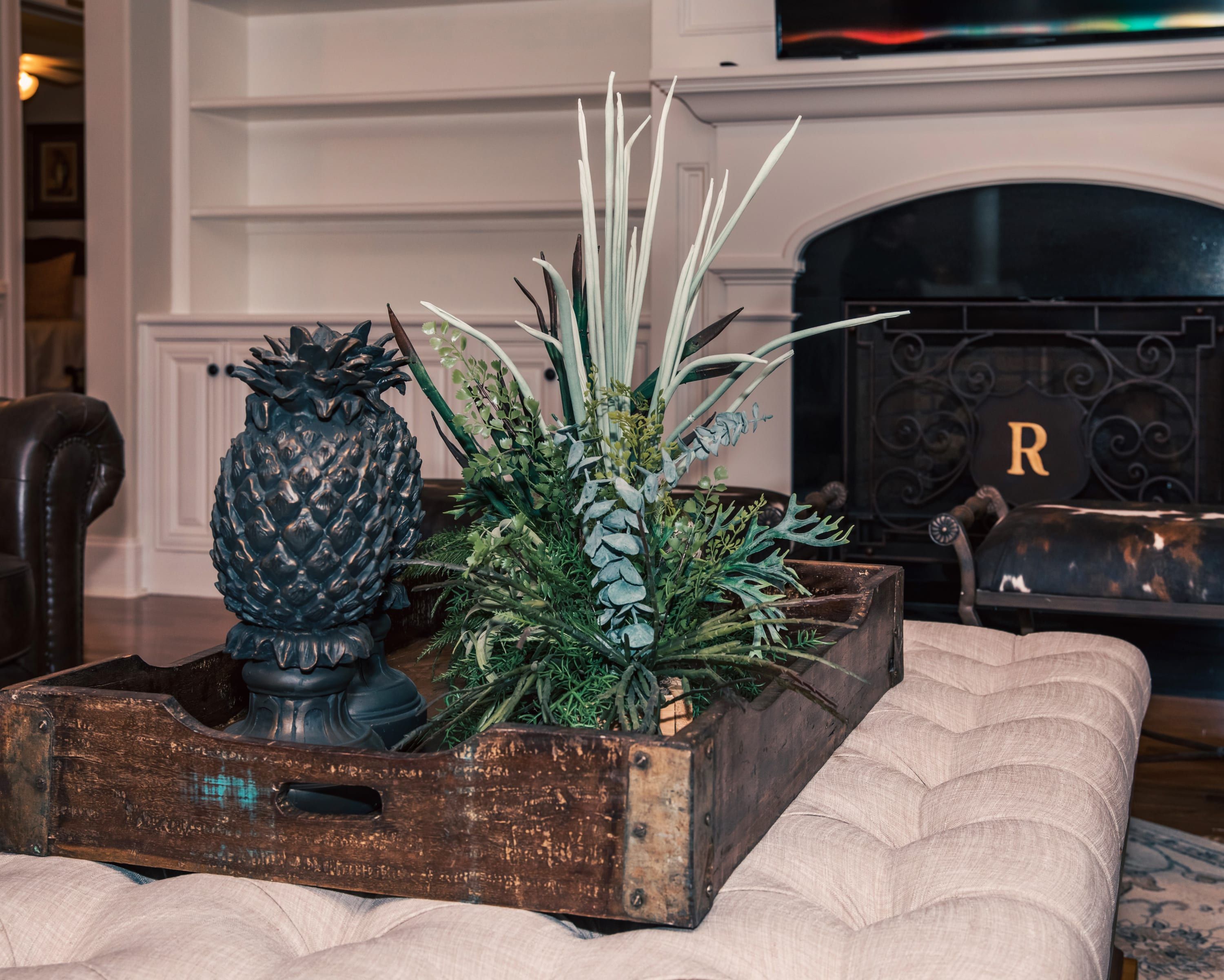 Een houten plantenbak in rustieke stijl met een dennenappel en groen blad op een met kussens beklede bank.