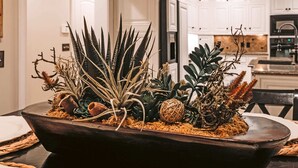 Un cuenco de madera oscura lleno de suculentas variadas y ramas decorativas sobre una mesa de comedor.