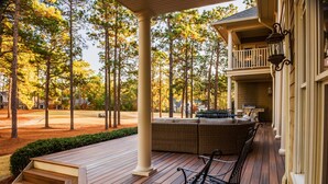 Un porche cubierto con terraza de madera, mobiliario exterior y vistas a un campo de golf.