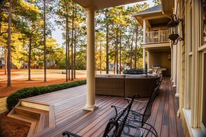 Eine überdachte Veranda mit Holzterrasse, Sitzgelegenheiten im Freien und Blick auf einen Golfplatz.