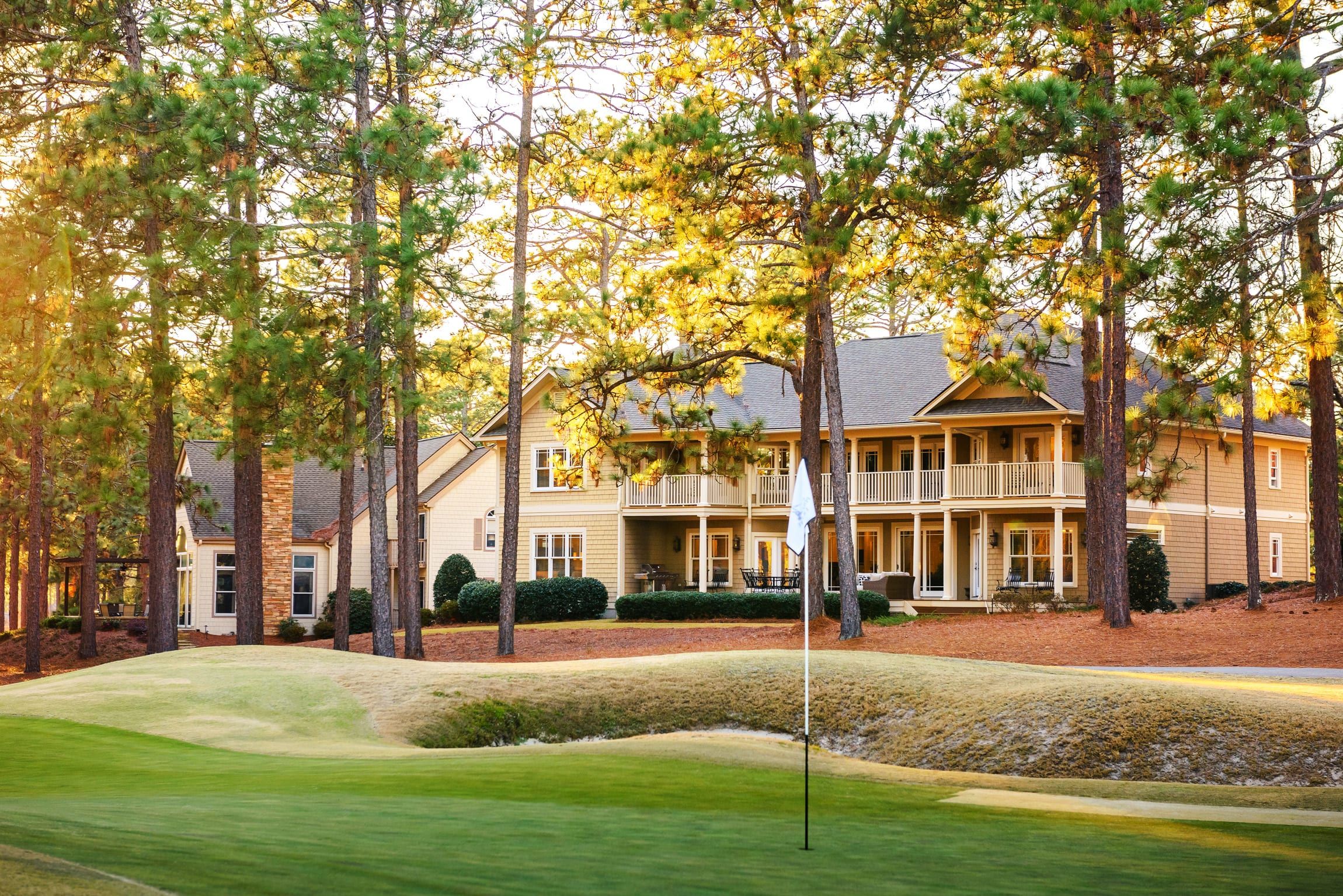 A two-story house with a front porch, surrounded by tall trees and a well-maintained lawn.