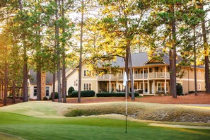 A two-story house with a front porch, surrounded by tall trees and a well-maintained lawn.