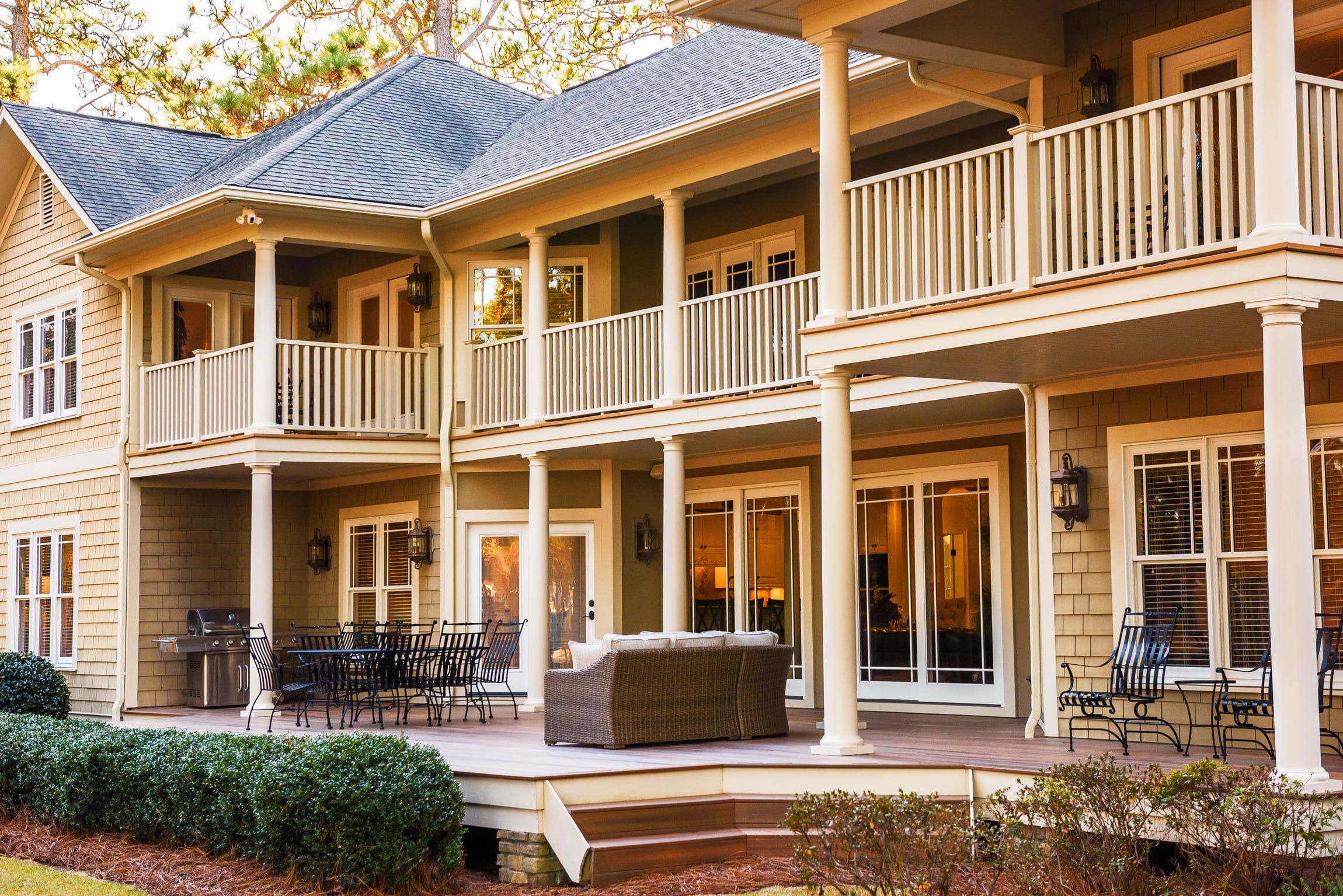 A two-story house with a covered porch, multiple balconies, and a patio area with outdoor furniture.