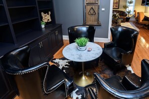 A room with a round table, two black leather chairs, a black leather ottoman, a cowhide rug, and a dark wooden cabinet with shelves.