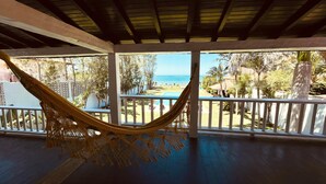 Eine Hängematte unter einer Holzbalkendecke mit Blick auf einen Pool und einen Strand.