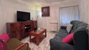 Un salon comprenant un téléviseur, un meuble en bois, une table basse, un canapé et un lustre.