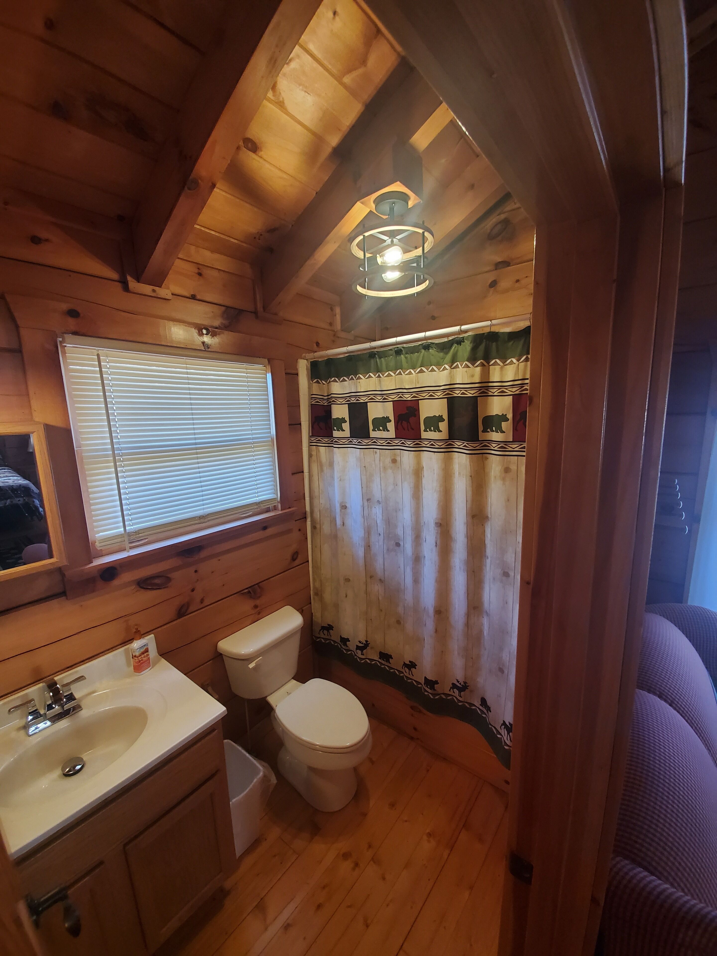 A wooden cabin bathroom with a window, toilet, sink, and a ceiling fan.