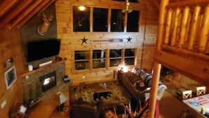 Interior de una cabaña de troncos con chimenea, paredes de madera, un televisor y una zona de estar acogedora.
