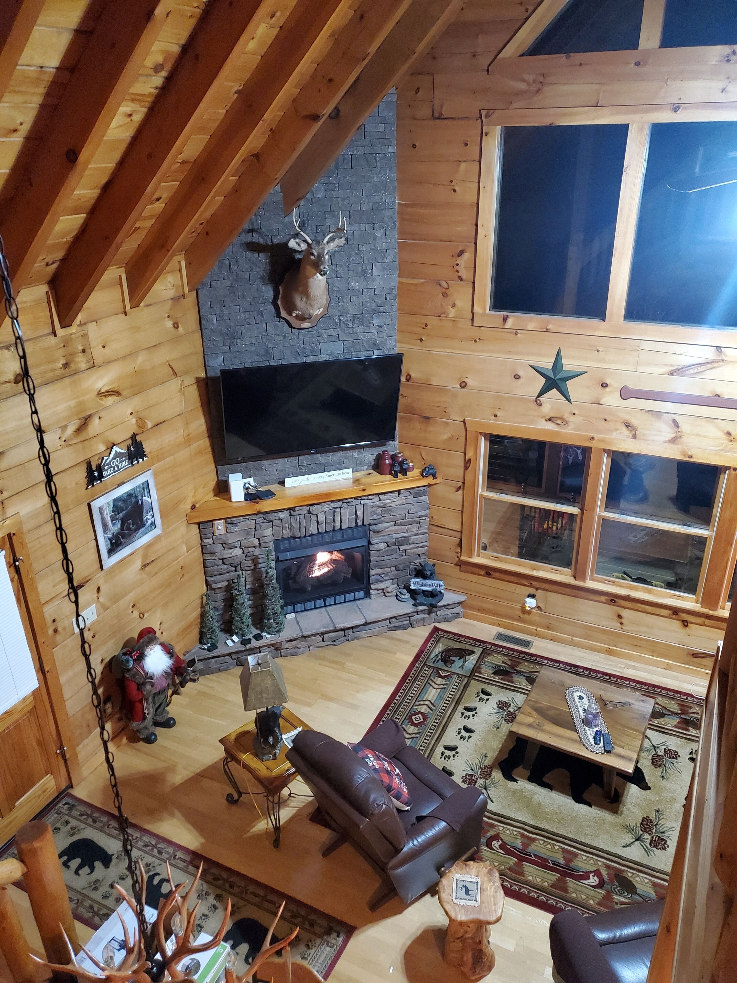 A cozy cabin interior with a stone fireplace, a mounted deer head, and a large window.