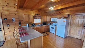 Cocina de cabaña de madera con una isla central, armarios de madera, una estufa, un refrigerador y un microondas.