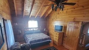 Una habitación de cabaña acogedora con cama, sofá, televisor y ventilador de techo.