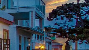 A multi-story building with balconies, a tree in the foreground, and a sunset in the background. - Mission Beach Steps to Beach Remodeled Home with AC, fireplace, and Parking (San Diego)