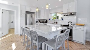 A modern kitchen with white cabinetry, a large island with bar stools, stainless steel appliances, and pendant lighting. - Mission Beach Steps to Beach Remodeled Home with AC, fireplace, and Parking (San Diego)