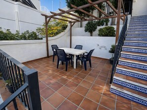 A patio with a white table and chairs, surrounded by a wooden pergola and potted plants.