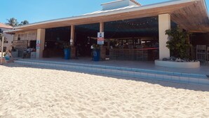 A beachside building with a covered outdoor seating area, a sign indicating mask requirements, and a sandy beach in the foreground. - Crystal Cove At Sapphire Beach (St Thomas)