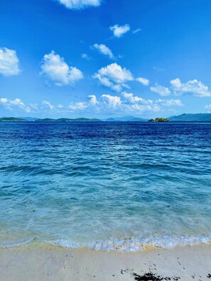 A beach with clear blue water, a sandy shore, and distant islands.