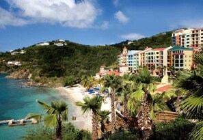 A coastal hotel with multiple colorful buildings, a beach, and palm trees.