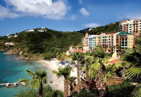 A coastal hotel with multiple colorful buildings, a beach, and palm trees.