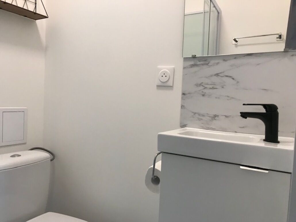 Et moderne badeværelse med toilet, vask og armatur i sort samt marmorbeklædt væg.