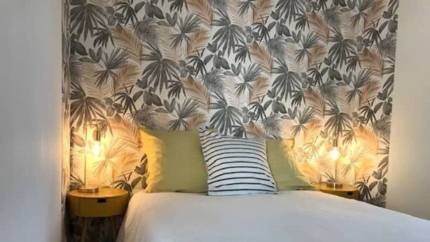 A bedroom with a bed, two bedside lamps, and a wall with a leaf pattern. - Cozy and bright studio for 2 (Mulhouse)