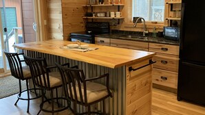 A kitchen with a wooden island, bar stools, a refrigerator, and wooden cabinetry. - Modern Cabin located between Grindstone and Lac Courte Oreilles (Hayward)