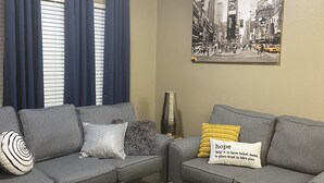 Un saló amb un sofà gris, un otomà negre, una taula de centre amb objectes decoratius, una catifa estampada i una pintura de paisatge urbà a la paret.