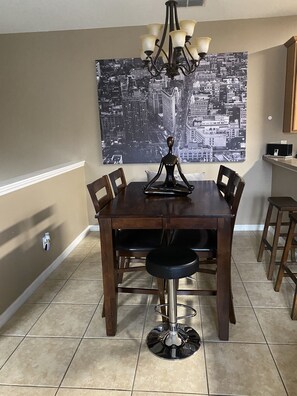 Un'area pranzo con un tavolo in legno scuro, quattro sedie, uno sgabello da bar e un quadro raffigurante un panorama urbano.