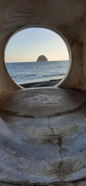 Une fenêtre circulaire offrant une vue sur la mer et une île lointaine.