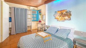 Une chambre à coucher avec un lit, un plafond en bois, un mur orné d’un tableau représentant un coucher de soleil, et une salle de bain avec un rideau de douche.