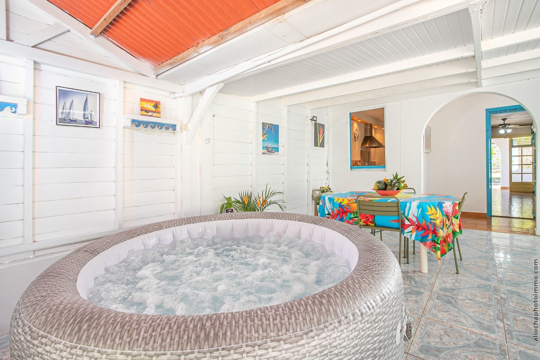Un espace détente avec un jacuzzi, une table à manger recouverte d’une nappe colorée et une vue sur l’extérieur.
