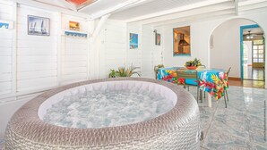 Un espace détente avec un jacuzzi, une table à manger recouverte d’une nappe colorée et une vue sur l’extérieur.