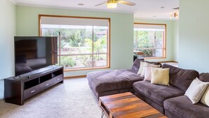 Un salon avec un téléviseur à écran plat posé sur un meuble en bois foncé, un canapé marron avec des coussins, une table basse en bois et un ventilateur de plafond.