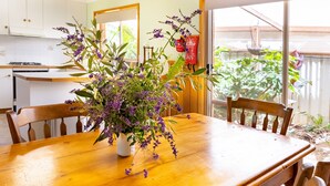 Une table à manger en bois sur laquelle est posé un vase blanc rempli de fleurs violettes.